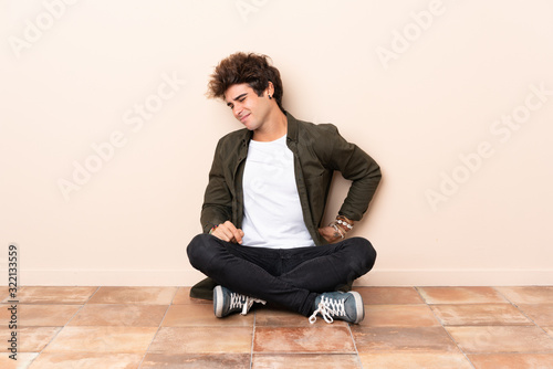 Young caucasian man sitting on the floor suffering from backache for having made an effort