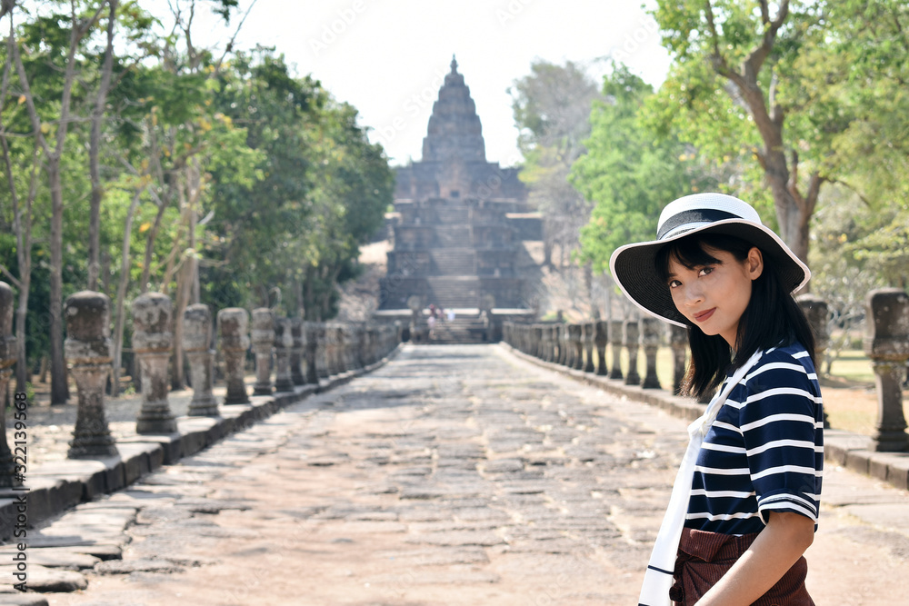 Young asian thai woman wearing а striped shirt and white hat posing in ancient khmer civilisation temple. Prasat Hin Phanom Rung, Thailand