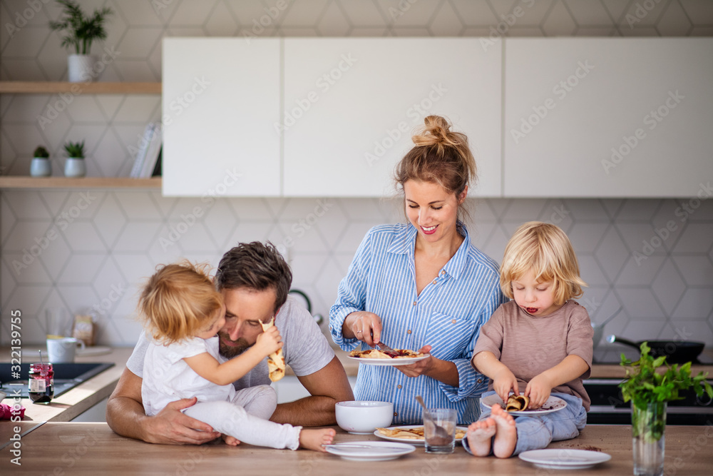 Young family with two small children indoors in kitchen, eating pancakes. Young family with two small children indoors in kitchen, eating pancakes.