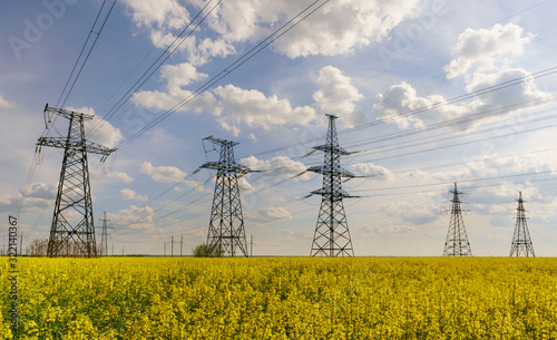 Power lines and high-voltage lines against the backdrop of blooming oilseed rape on a summer day.