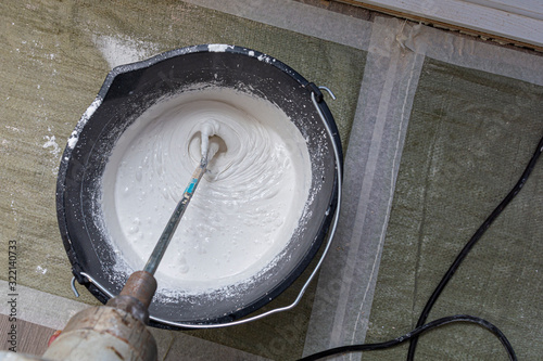 Worker mixing plaster in a bucket for alignment and putty walls of the apartment using an electric drill, close-up. Worker mixes construction putty in a bucket.