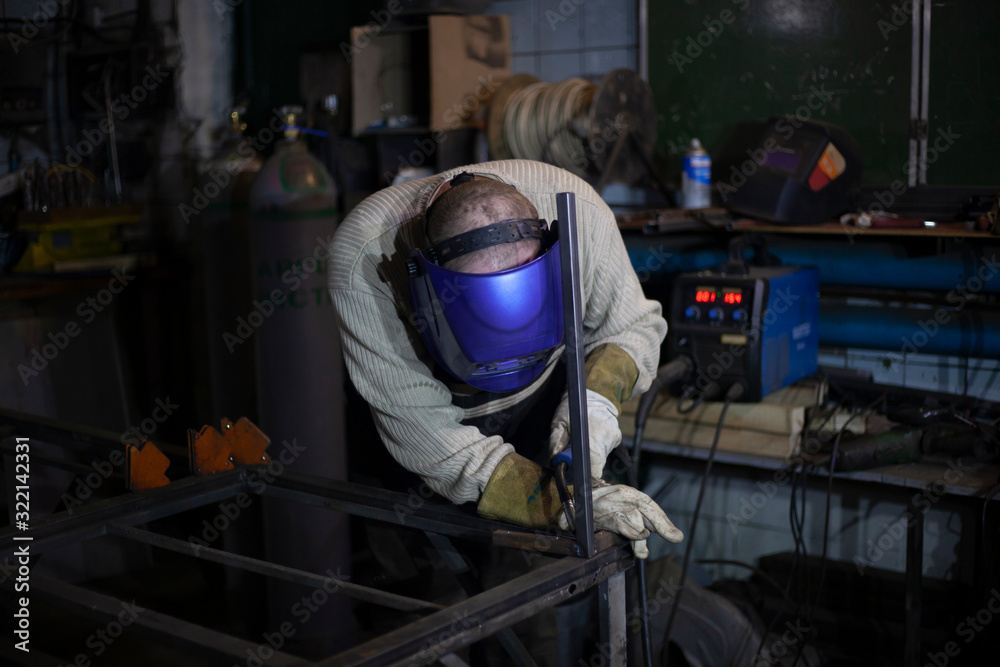 Welder at work. The welder heats the metal. Classes in the workshop. Steel processing. Welder in a blue welding mask. High melting point of metal. A man doing hard work.