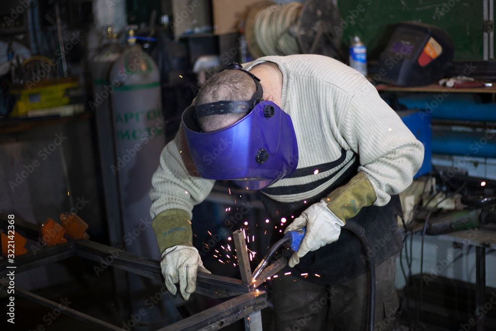 Welder at work. The welder heats the metal. Classes in the workshop. Steel processing. Welder in a blue welding mask. High melting point of metal. A man doing hard work. Welder at work. The welder heats the metal. Classes in the workshop. Steel processing. Welder in a blue welding mask. High melting point of metal. A man doing hard work.
