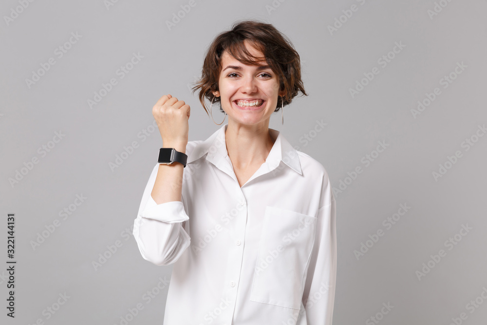 Smiling funny young business woman in white shirt posing isolated on grey wall background studio portrait. Achievement career wealth business concept. Mock up copy space. Wearing smart watch on hand. Smiling funny young business woman in white shirt posing isolated on grey wall background studio portrait. Achievement career wealth business concept. Mock up copy space. Wearing smart watch on hand.