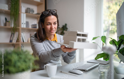 Architect with model of a house sitting at the desk indoors in office. photo