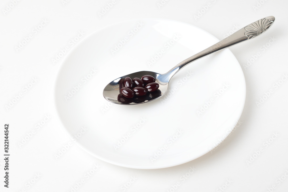 Astaxanthin capsules in the spoon on a white plate background. Astaxanthin capsules in the spoon on a white plate background.