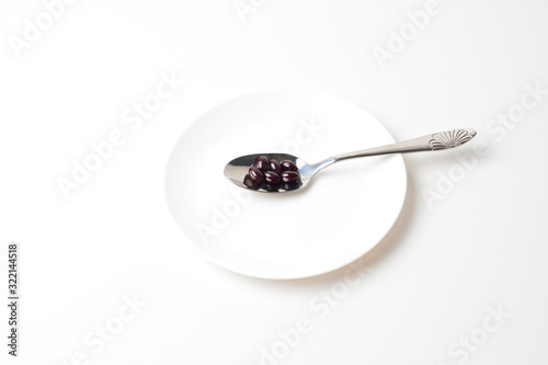 Astaxanthin capsules in the spoon on a white plate background. Top view.