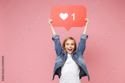 Funny little kid girl 12-13 years old in denim jacket isolated on pastel pink wall background in studio. Childhood lifestyle concept. Mock up copy space. Hold huge like sign from Instagram heart form.