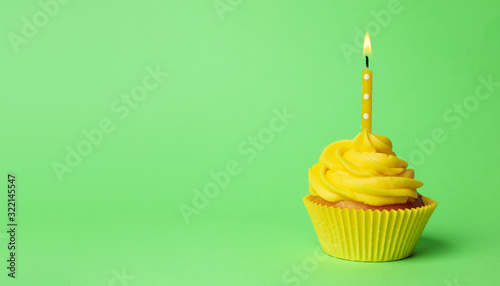 Delicious birthday cupcake with yellow cream and burning candle on green background. Space for text