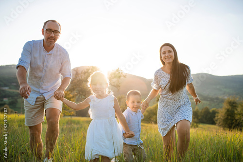 Young family with two small children running on meadow outdoors at sunset.