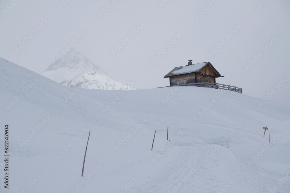 Beautiful view of lonely small wooden house in snowy mountains in foggy winter day, when all around is white. Around Alpe di Nemes refuge in Sexten Dolomites, South Tyrol, Italy