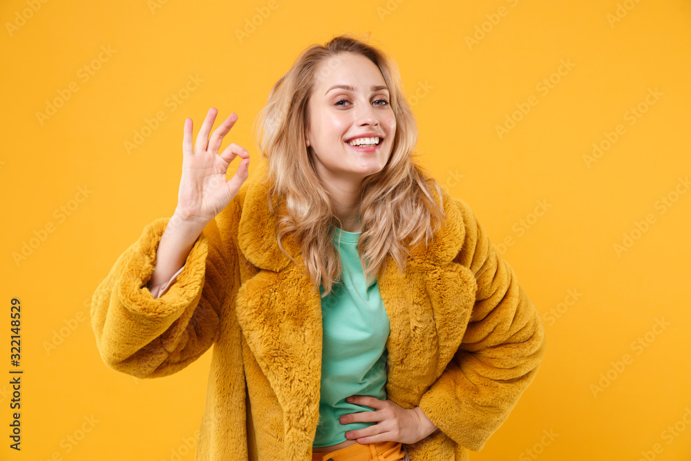 Smiling beautiful young blonde woman girl in yellow fur coat posing isolated on orange background studio portrait. People sincere emotions lifestyle concept. Mock up copy space. Showing OK gesture. Smiling beautiful young blonde woman girl in yellow fur coat posing isolated on orange background studio portrait. People sincere emotions lifestyle concept. Mock up copy space. Showing OK gesture.