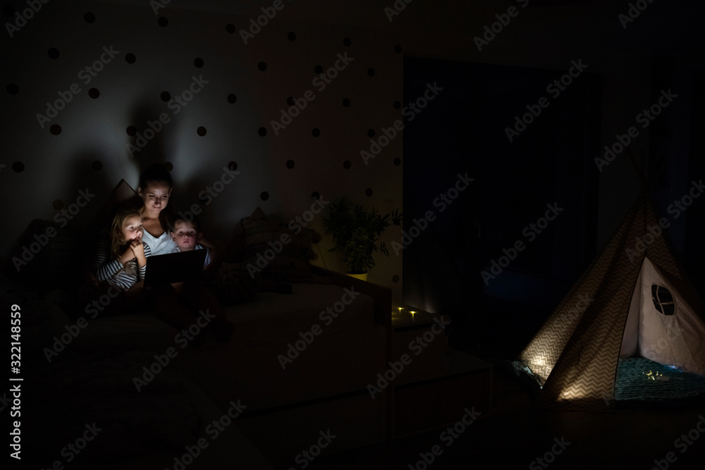 Young mother with children sitting indoors in bedroom, using laptop.