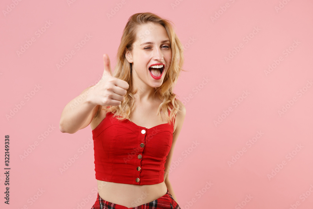 Cheerful young woman girl in red sexy clothes posing isolated on pastel pink background studio portrait. People sincere emotions lifestyle concept. Mock up copy space. Showing thumbs up, blinking. Cheerful young woman girl in red sexy clothes posing isolated on pastel pink background studio portrait. People sincere emotions lifestyle concept. Mock up copy space. Showing thumbs up, blinking.