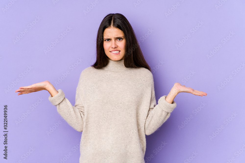 Young caucasian woman isolated on purple background confused and doubtful shrugging shoulders to hold a copy space. Young caucasian woman isolated on purple background confused and doubtful shrugging shoulders to hold a copy space.