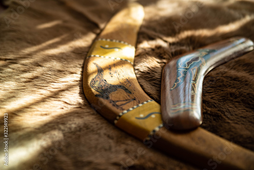 Two old boomerangs laying on the kangaroo skin, fur with wooden glossy table in the background. Souvenirs from Australia on display, shallow depth of field, warm colors