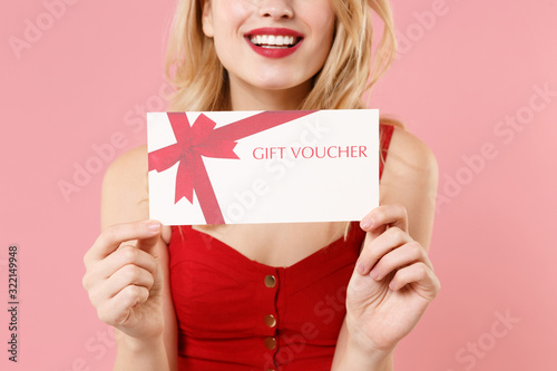 Cropped image of young blonde woman girl in red sexy clothes isolated on pastel pink background studio portrait. People sincere emotions lifestyle concept. Mock up copy space. Hold gift certificate.