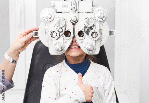 Girl shows thumb up at an ophthalmologist's appointment. Foropter - a device for measuring refractive error and for determining information for a prescription for glasses photo