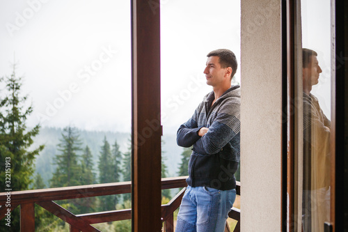 A young man in the morning looks from the hotel balcony with a view of the mountains, the fog and the fir forest. Mountain views at the Pamporovo hotel in Bulgaria in a ski resort
