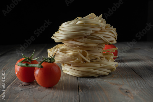 raw egg noodles with tomatoes stacked on wood photo