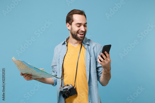 Smiling traveler tourist man in yellow clothes with photo camera isolated on blue background. Passenger traveling on weekends. Air flight journey. Hold city map mobile phone with blank empty screen. photo