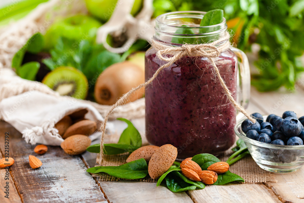 Healthy food and vegan diet concept - mason jar of fresh juice or smoothie with blueberry, spinach, banana, almond milk. Antioxidant detox beverage with raw ingredients. Close up, wooden background. Healthy food and vegan diet concept - mason jar of fresh juice or smoothie with blueberry, spinach, banana, almond milk. Antioxidant detox beverage with raw ingredients. Close up, wooden background.