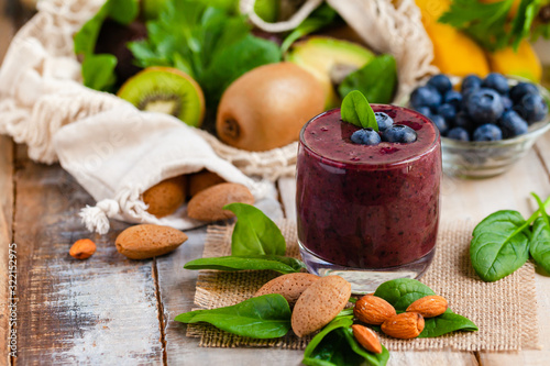 Healthy food and vegan diet concept - fresh juice or smoothie with blueberry, spinach, banana, kiwi, almond milk. Tasty detox beverage with raw ingredients.  Wooden background, close up, macro