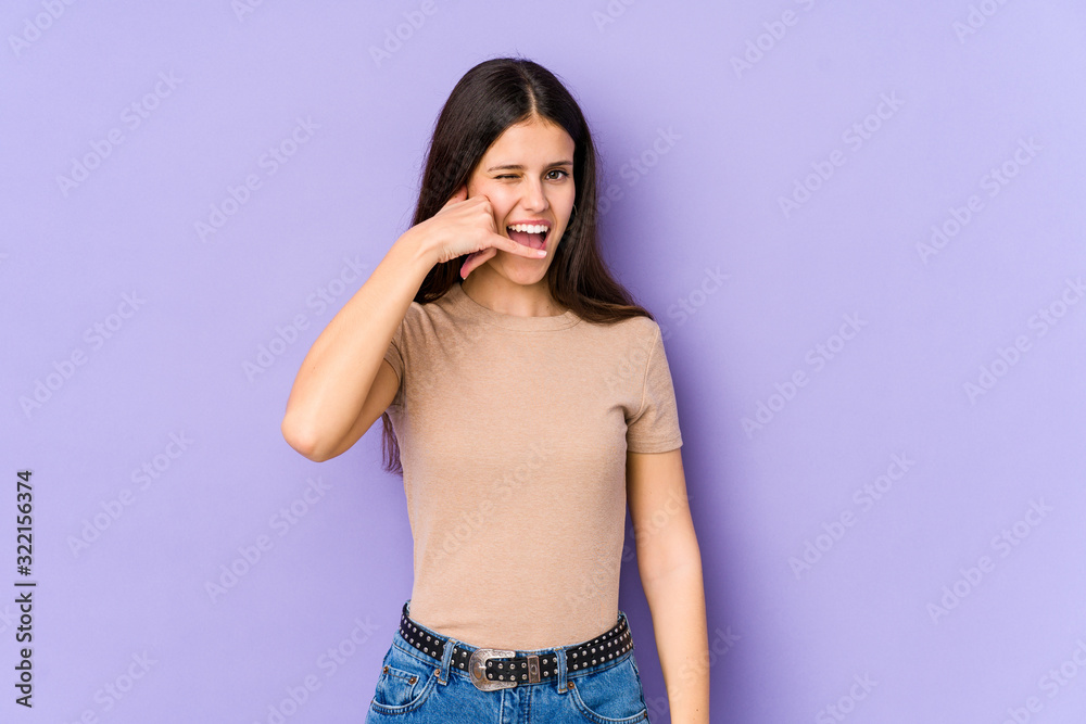 Young caucasian woman isolated on purple background showing a mobile phone call gesture with fingers. Young caucasian woman isolated on purple background showing a mobile phone call gesture with fingers.