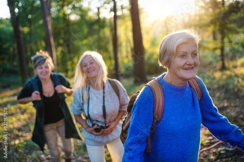 Senior women friends with camera walking outdoors in forest. © Halfpoint