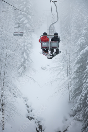 Two snowboarders sitting on the ski chair lift. Ski lift in the forest. Extreme snow conditions, Korbielow village, Poland photo