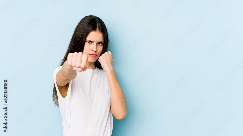Young caucasian woman isolated on blue background throwing a punch, anger, fighting due to an argument, boxing. Young caucasian woman isolated on blue background throwing a punch, anger, fighting due to an argument, boxing.