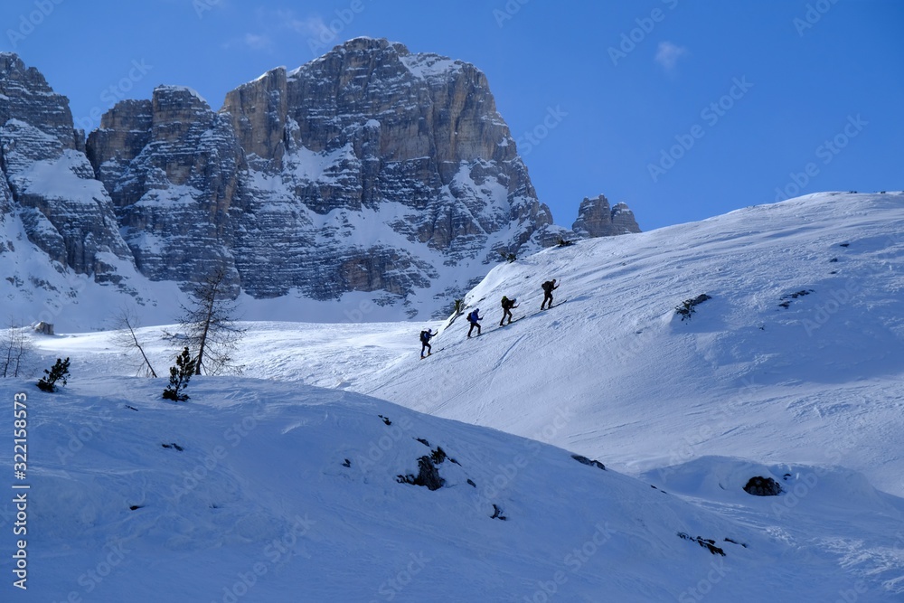 A group of skiers climbing on backcountry skis through snowy mountains on a sunny day. During trip in Dolomites around Tre Cime. Sexten Dolomites, South Tyrol, Italy