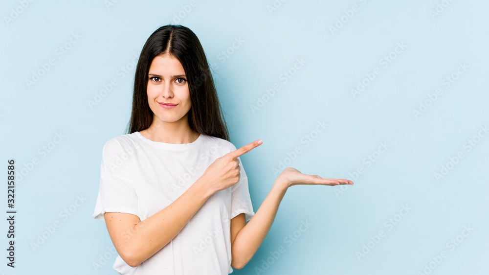 Young caucasian woman isolated on blue background excited holding a copy space on palm. Young caucasian woman isolated on blue background excited holding a copy space on palm.
