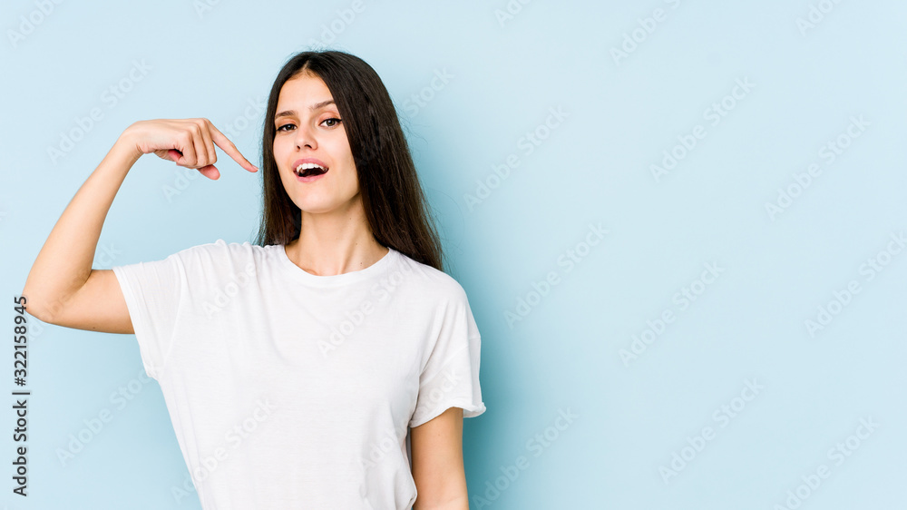 Fototapeta premium Young caucasian woman isolated on blue background person pointing by hand to a shirt copy space, proud and confident