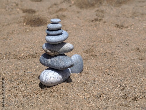 A stone pyramid on fine sand made of flat and round stones. Summer calm background.