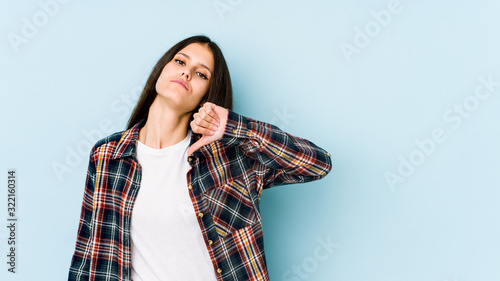 Young caucasian woman isolated on blue background showing a dislike gesture, thumbs down. Disagreement concept. © Asier
