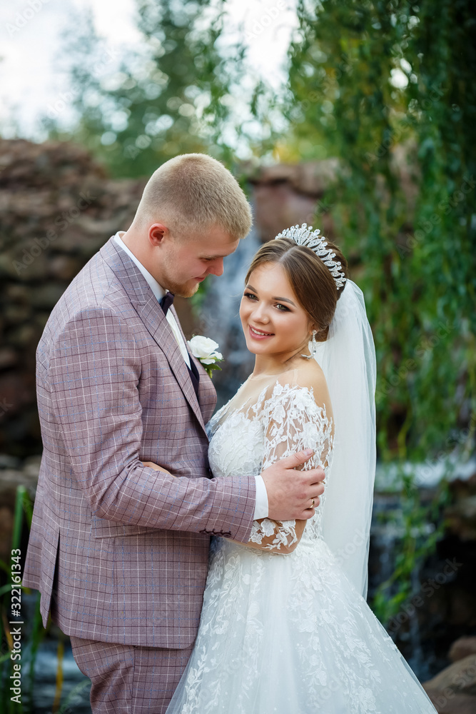 Bride in white dress and groom in costume cuddle and walk in the park Bride in white dress and groom in costume cuddle and walk in the park