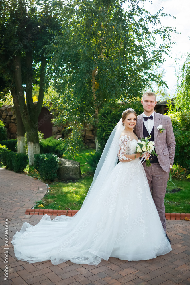 Bride in white dress and groom in costume cuddle and walk in the park