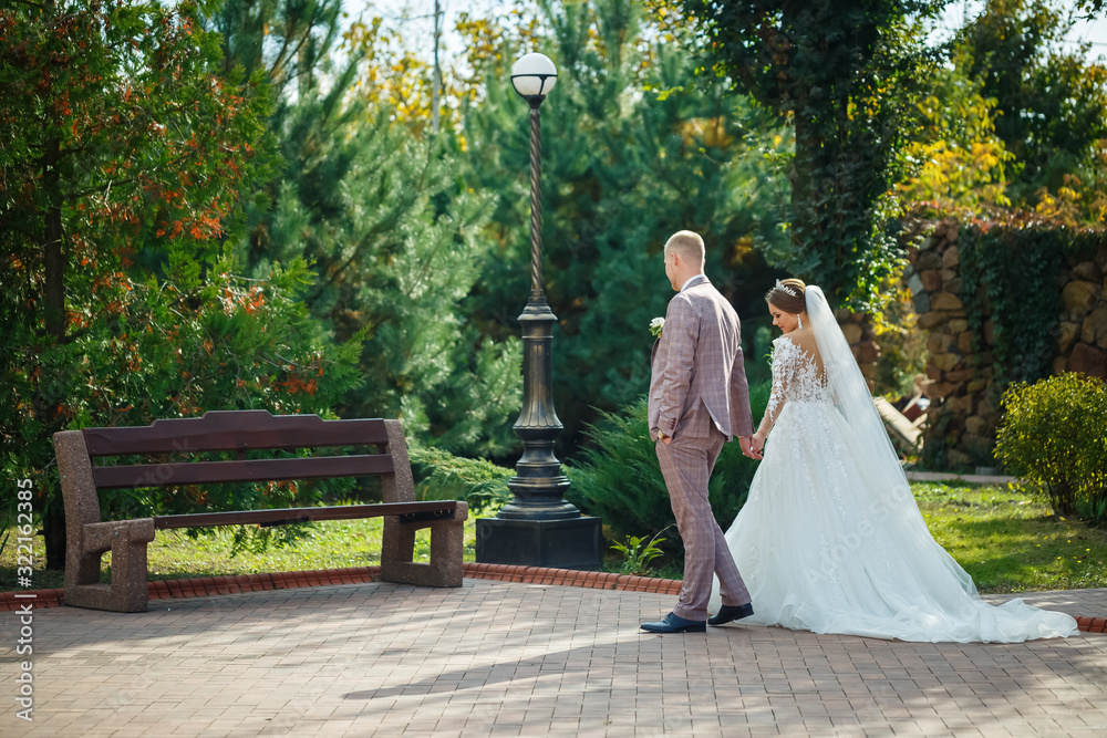 Bride in white dress and groom in costume cuddle and walk in the park