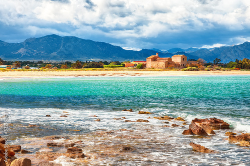 The Nora bay and beach, the medieval Sant'Efisio church near the shore and mountains in the background photo