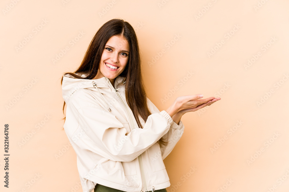 Young caucasian woman isolated on beige background holding a copy space on a palm. Young caucasian woman isolated on beige background holding a copy space on a palm.