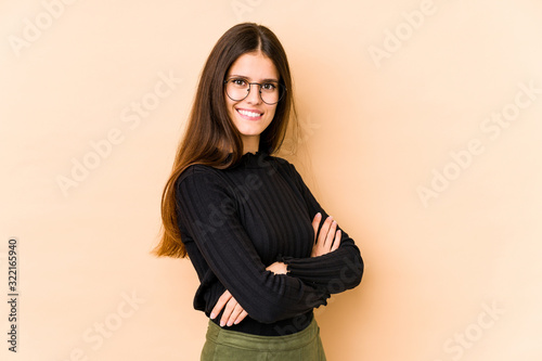 Young caucasian woman isolated on beige background who feels confident, crossing arms with determination. © Asier