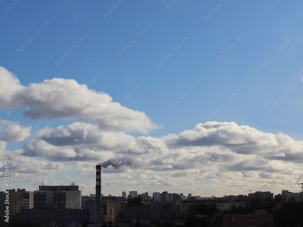 A factory chimney emits clouds of smoke that are mixed with ordinary clouds. The theme of ecology and nature.