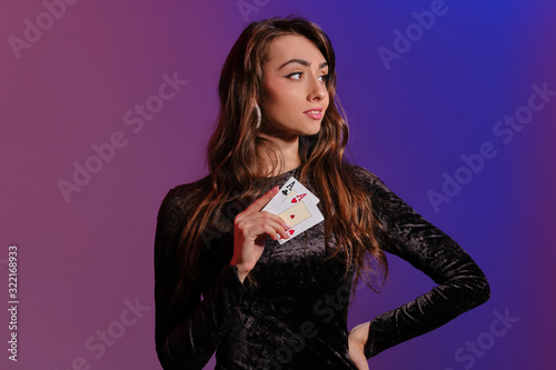 Brunette woman in black velvet dress showing two playing cards, posing against coloful background. Gambling entertainment, poker, casino. Close-up.