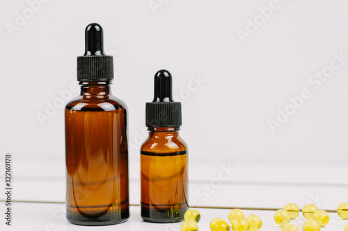 Moisturizing and healing skin serum with vitamin C on a white wooden background. Vitamin capsules as a supplement to a cream or essence for home care