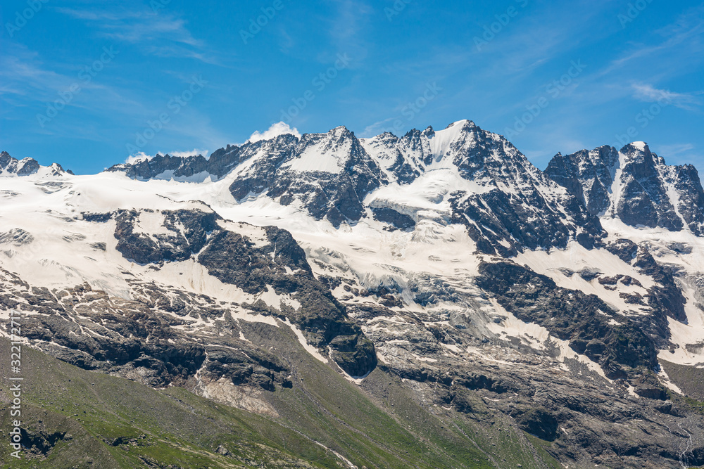 Spectacular mountain panorama with peaks and slopes covered with glaciers above lush green valley.