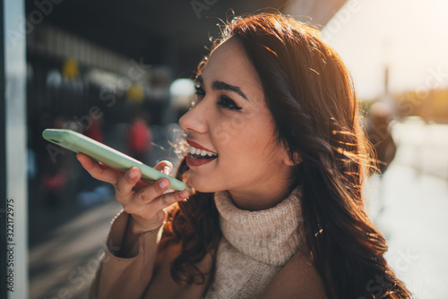 Young hispanic positive woman holding smartphone speak activate virtual digital voice assistant, Cheerful hipster girl using easy voice messaging to talking with friend on cellphone outdoors photo