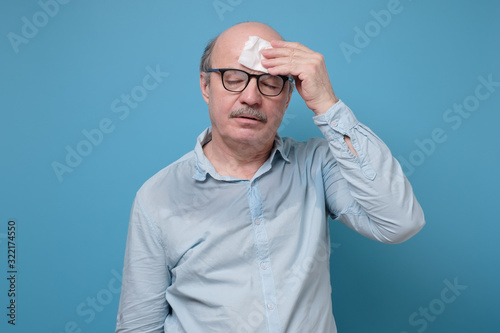 Senior hispanic man with sweat stain on his shirt suffering from hot weather. Studio shot on blue wall. Problem with hyperhidrosis photo