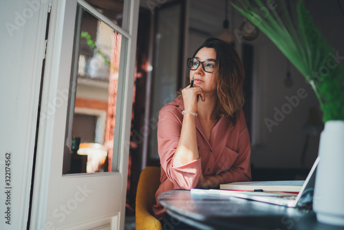 Beautiful caucasian woman dreaming about something while sitting with portable net-book in modern office, young female freelancer thinking about new ideas during work on laptop computer