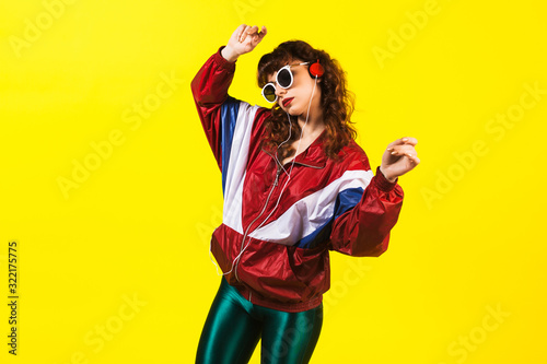 Cheerful gorgeous girl in clothes in the style of the 90s, with a vintage cassette player and headphones, in the studio on a white background. Music, emotions, fashion